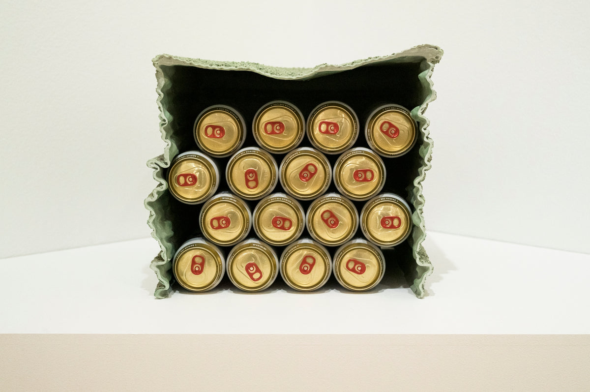 00_19 by Nick Patterson. Gold drink cans with red pull tabs stacked in a corrugated holder.