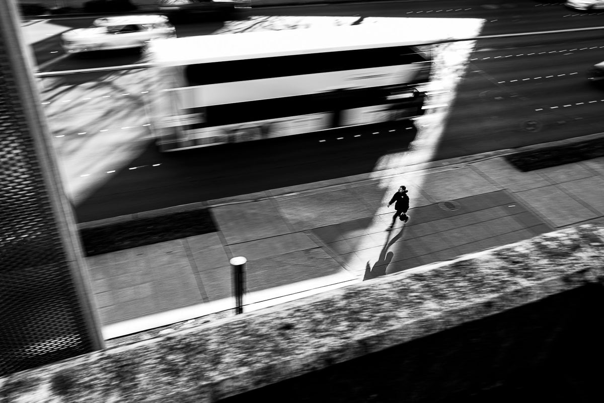 00_39 by Nick Patterson. A figure beside a passing vehicle on a city street in black and white.