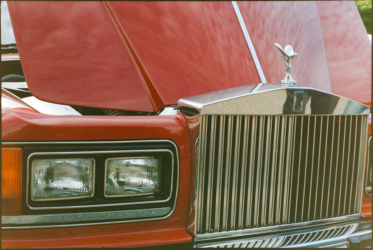 00_20 by Nick Patterson. The chrome grille and hood ornament of a red classic car.