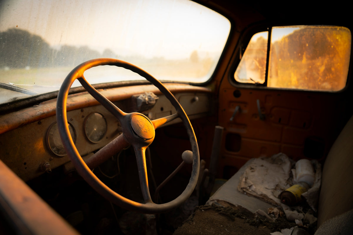 00_18 by Nick Patterson. An old vehicle's steering wheel and dashboard in warm light.