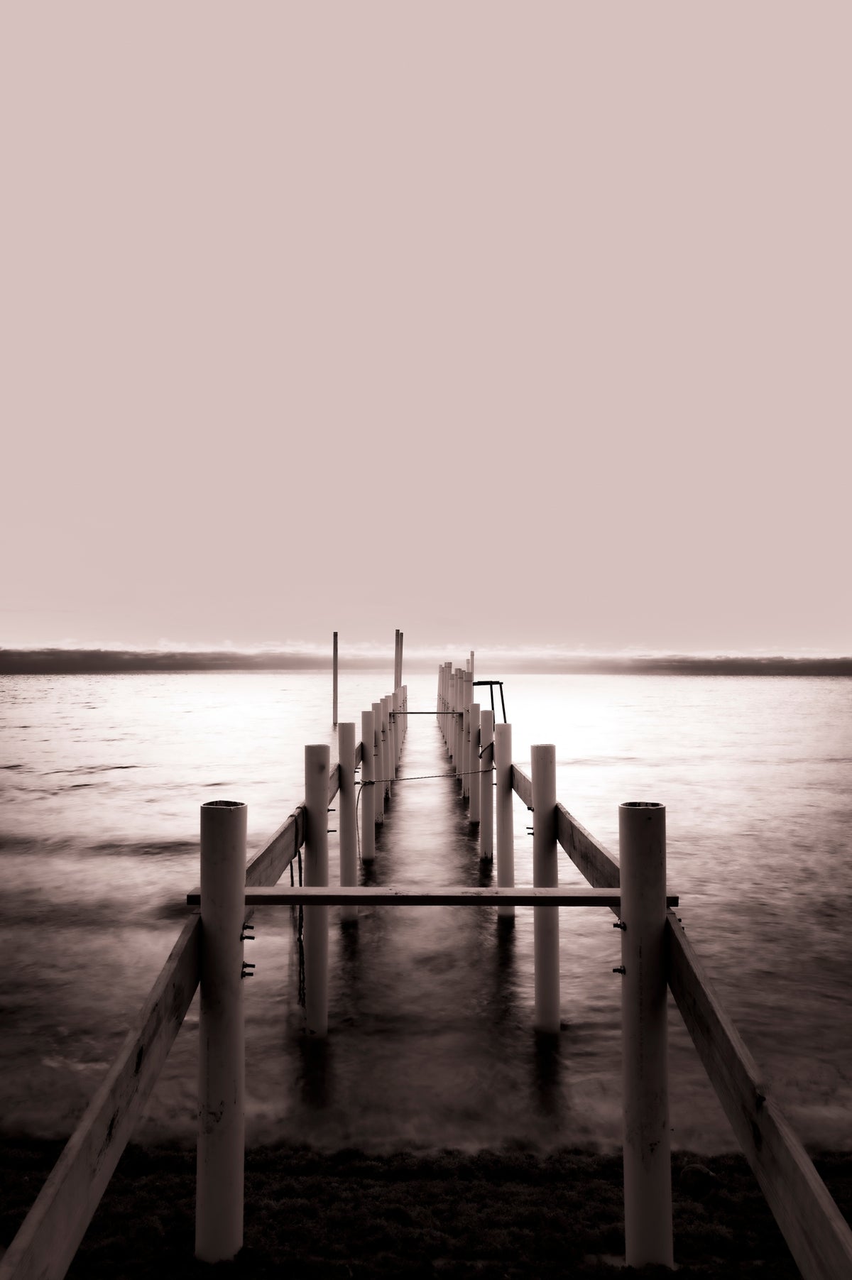 00_02 by Nick Patterson. A wooden pier reaching across still water beneath a pale sky.