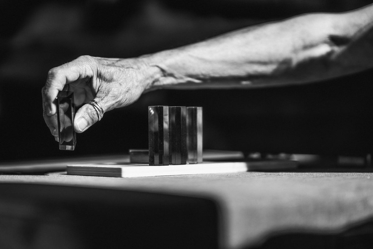 00_10 by Nick Patterson. A hand reaching across a table beside a glass in black and white.