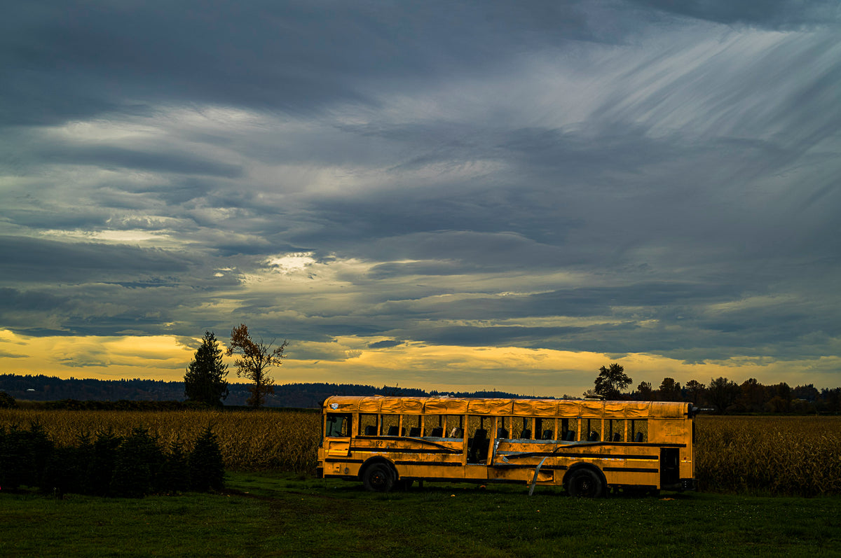 00_31 by Nick Patterson. A yellow school bus in a field beneath a dramatic evening sky.