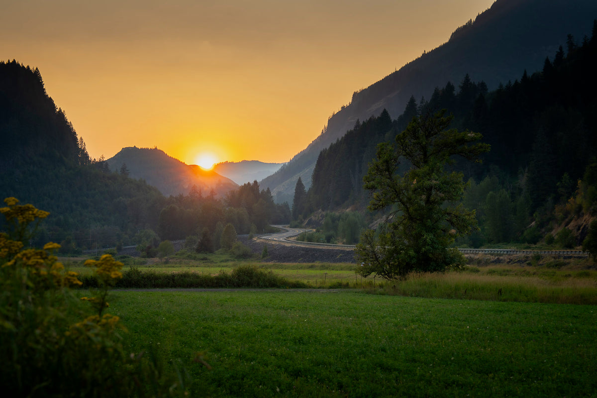 00_42 by Nick Patterson. The sun setting between mountains above a green valley.