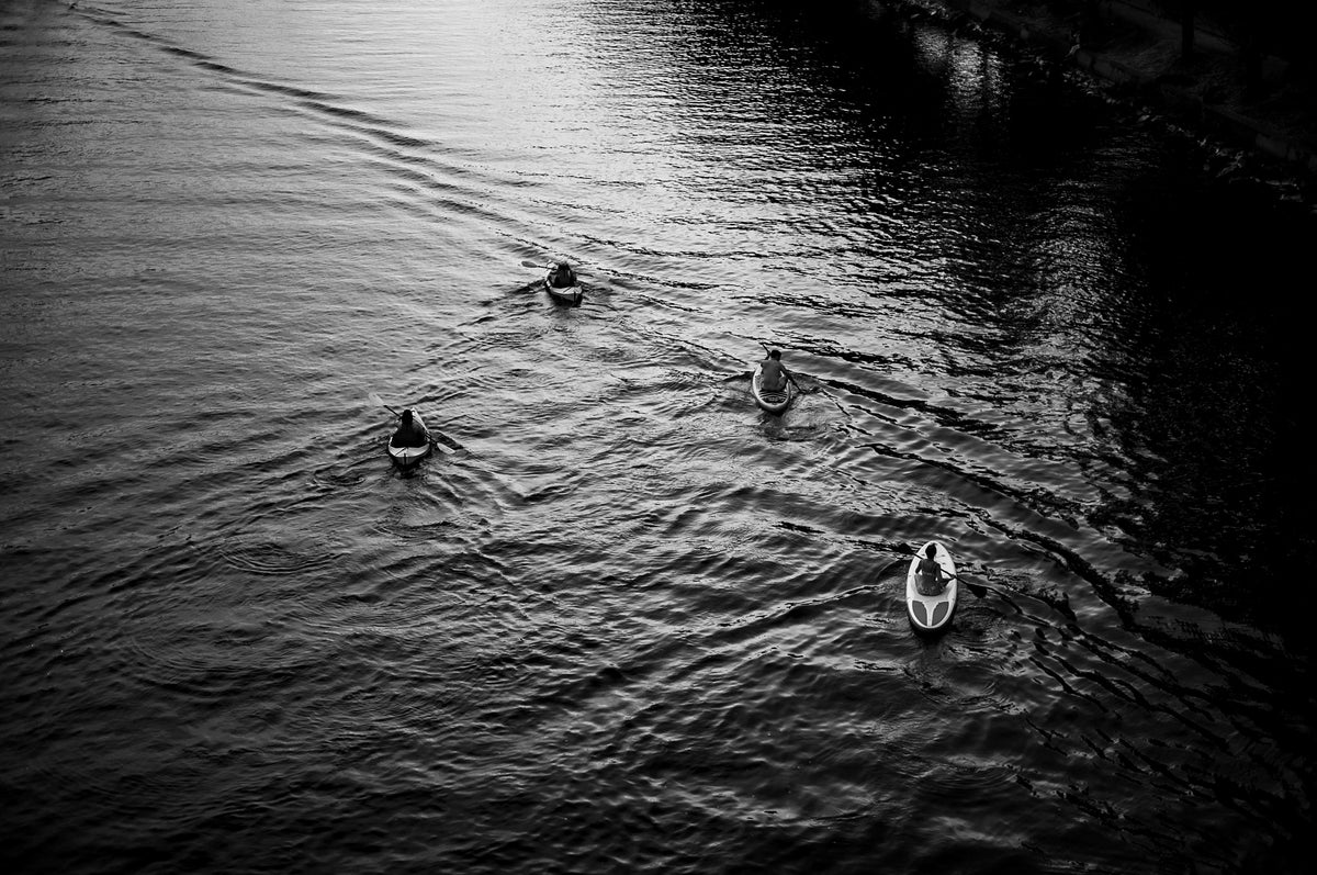 00_25 by Nick Patterson. Four paddlers making wakes across dark water, photographed in black and white.