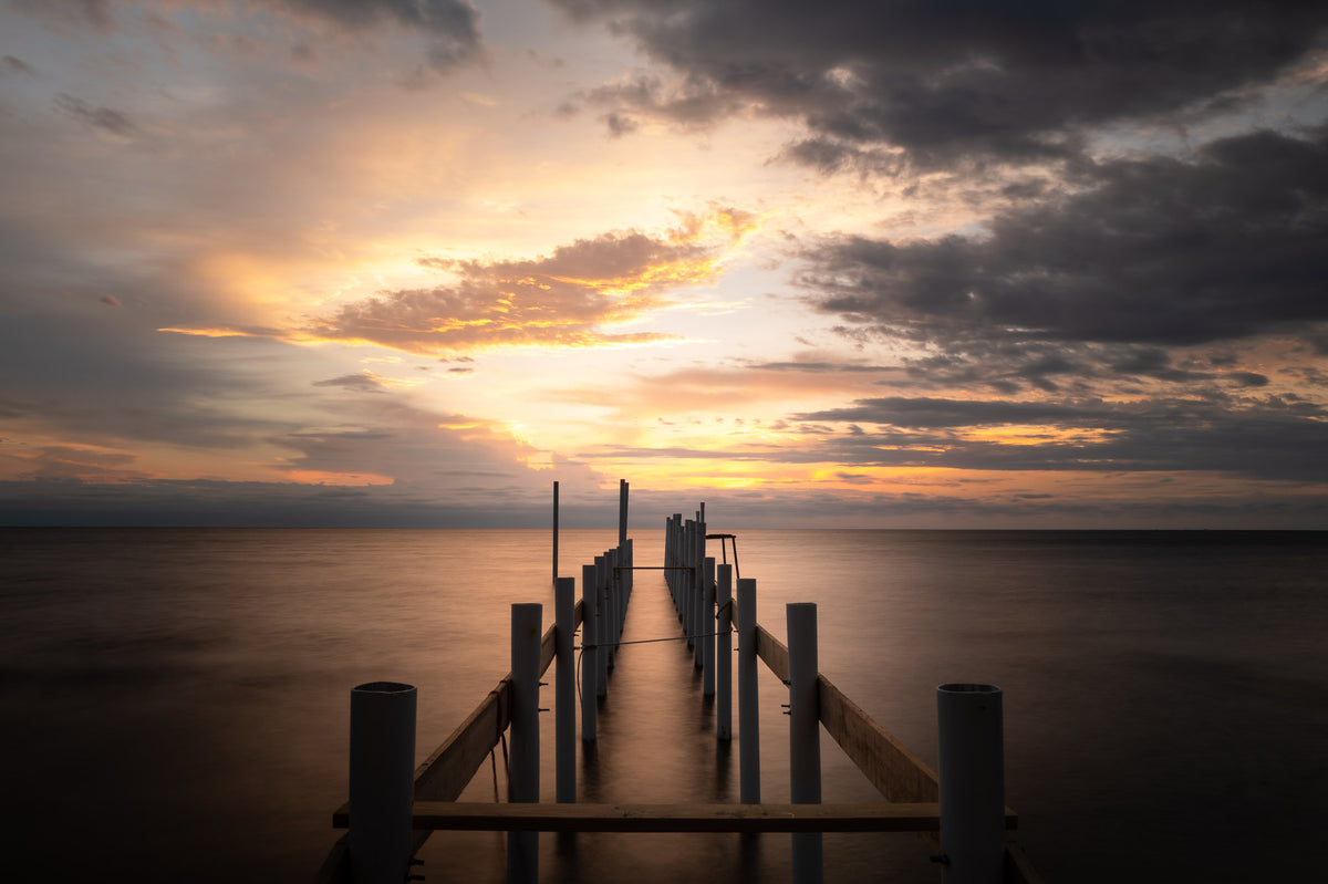 00_07 by Nick Patterson. A wooden pier beneath clouds and a glowing golden sky.