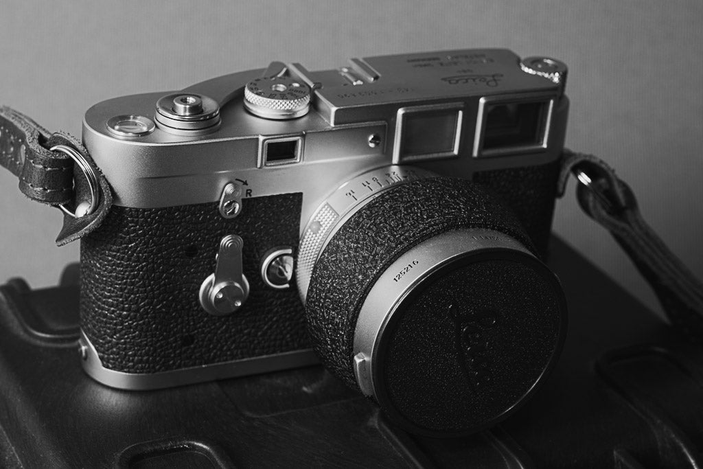 Black-and-white front view of the Leica M3 with lens hood and cap.