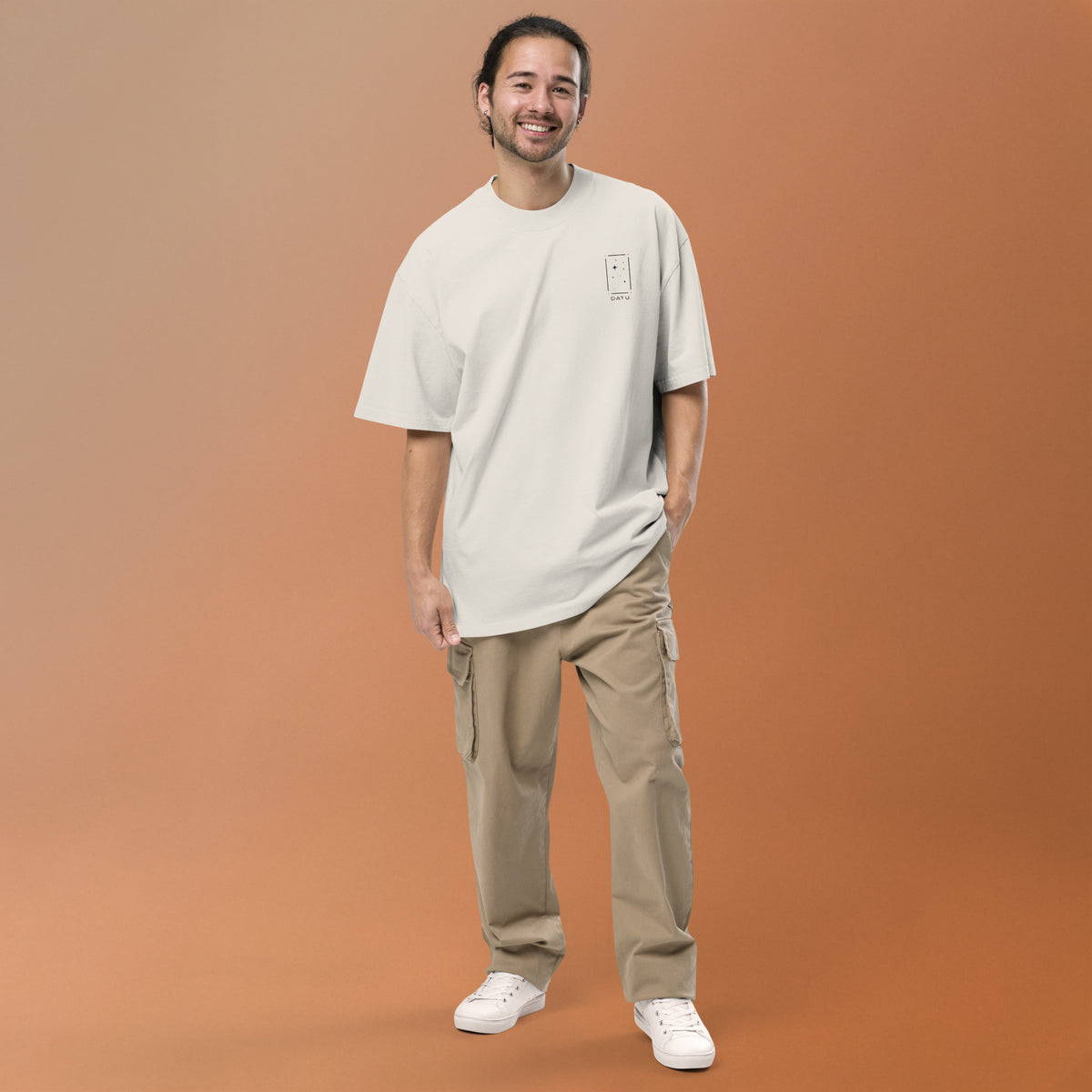 DATU Studio Tee in faded bone, worn with neutral trousers against a warm clay backdrop.